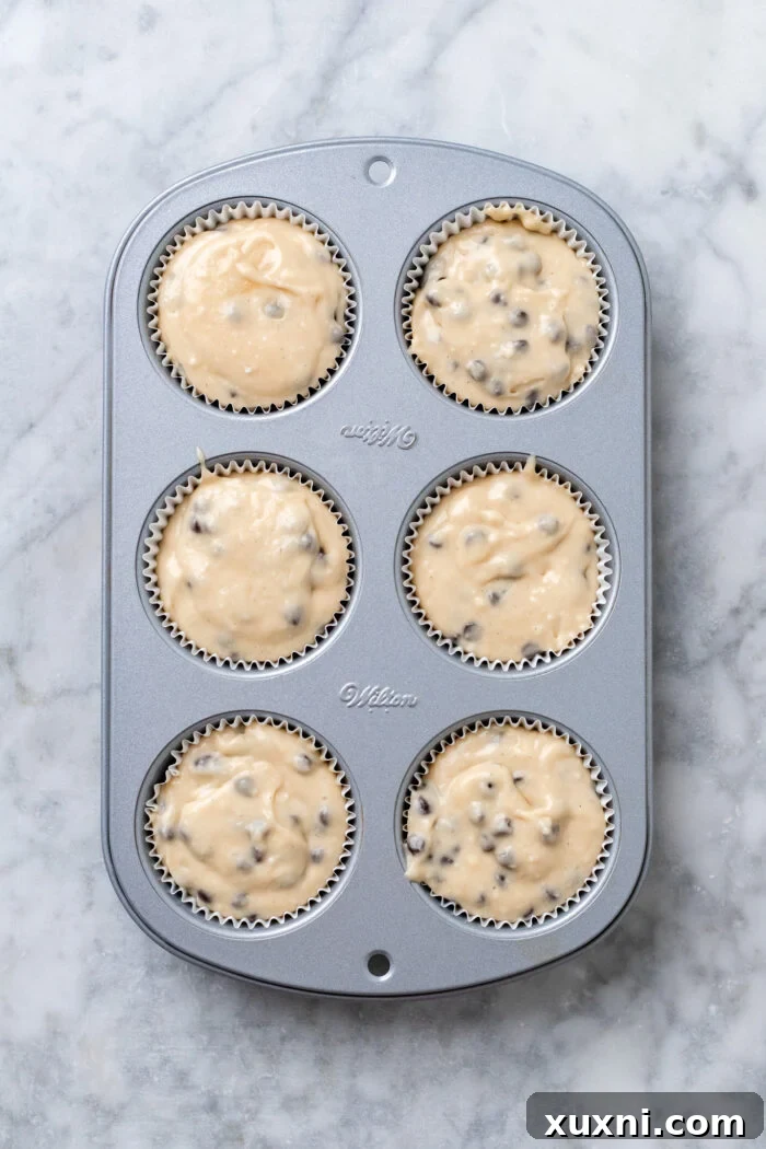 Cupcake liners filled with batter in a muffin tin, ready for baking.