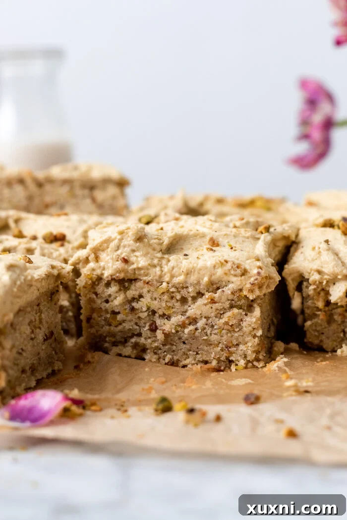 A close-up of a single slice of vegan pistachio cake, highlighting its texture and frosting.