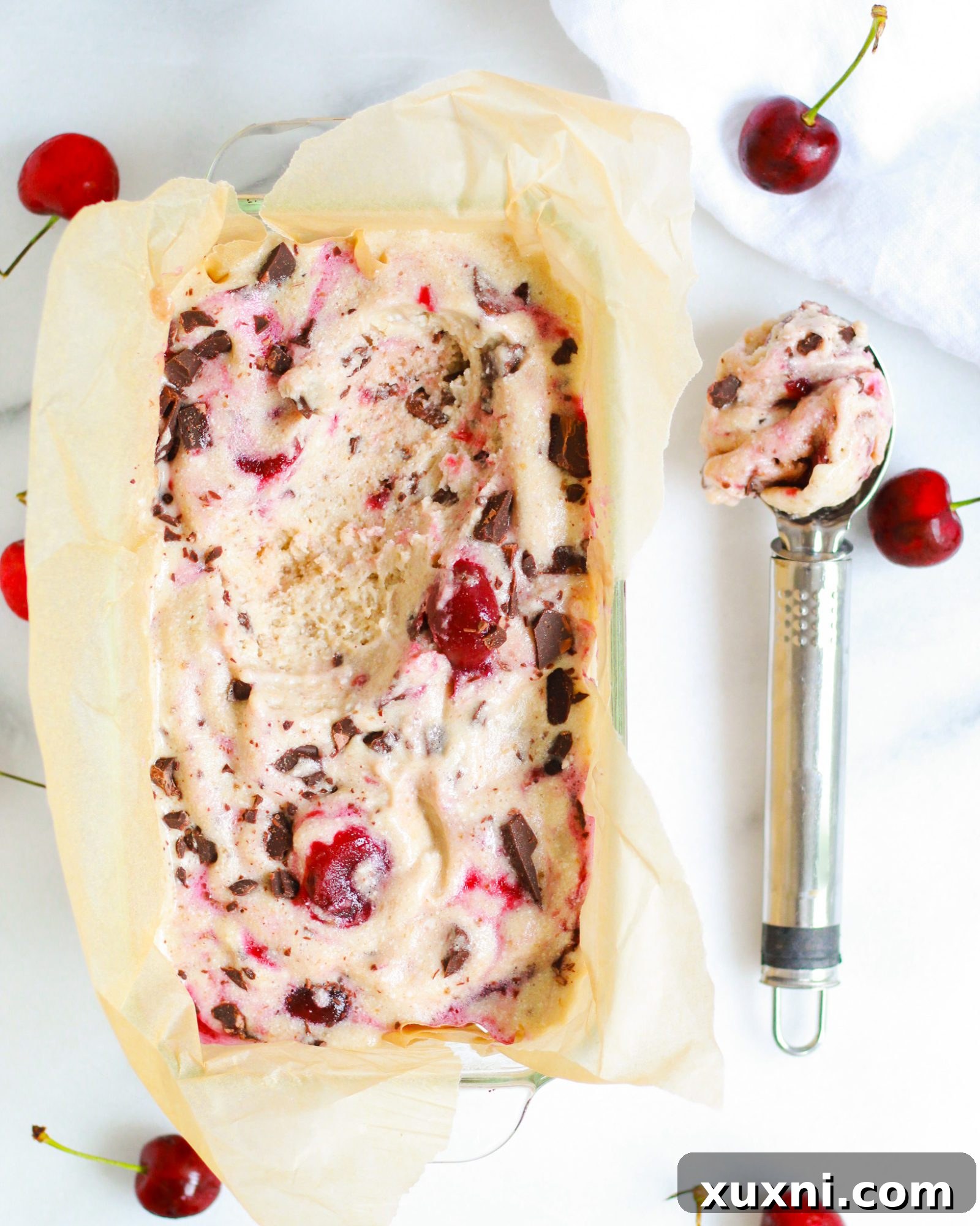 scoop of vegan cherry ice cream next to ice cream container