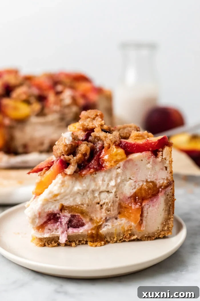 Slice of vegan peach cobbler cheesecake on a plate, showcasing its creamy layers and golden crumble topping.