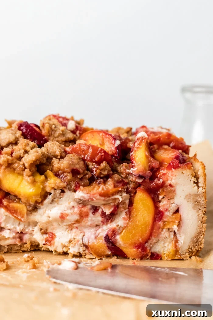 Beautifully sliced vegan peach cobbler cheesecake, displaying its distinct layers of crust, cheesecake, peaches, and crumble.