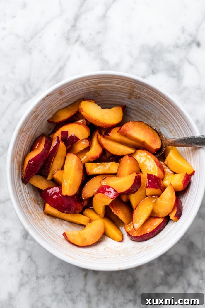 Fresh peach slices in a bowl, coated with spices and ready for roasting.