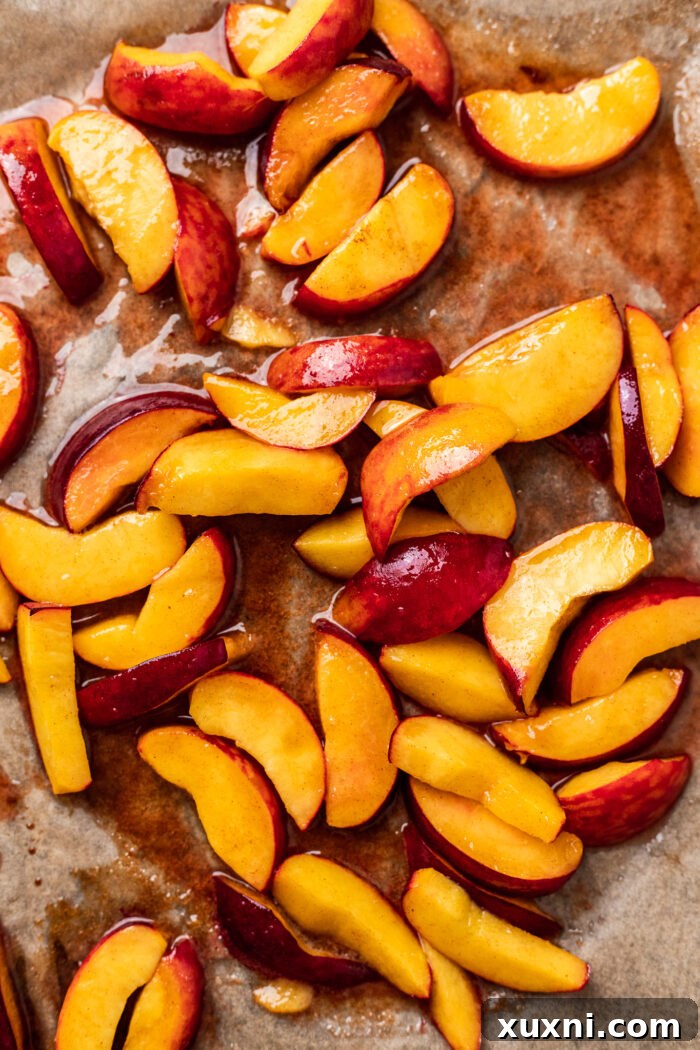 Roasted peaches, glistening with juices and caramelization, on a baking sheet.
