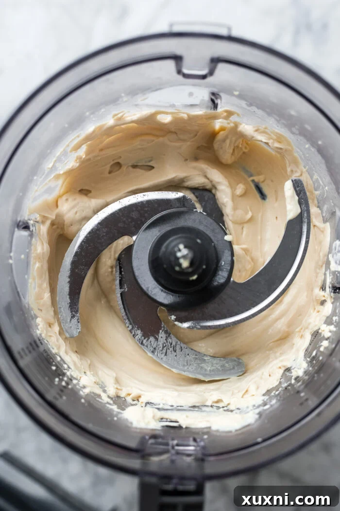 Smooth, blended vegan cream cheese rotating in a food processor bowl, showing its perfectly creamy consistency.