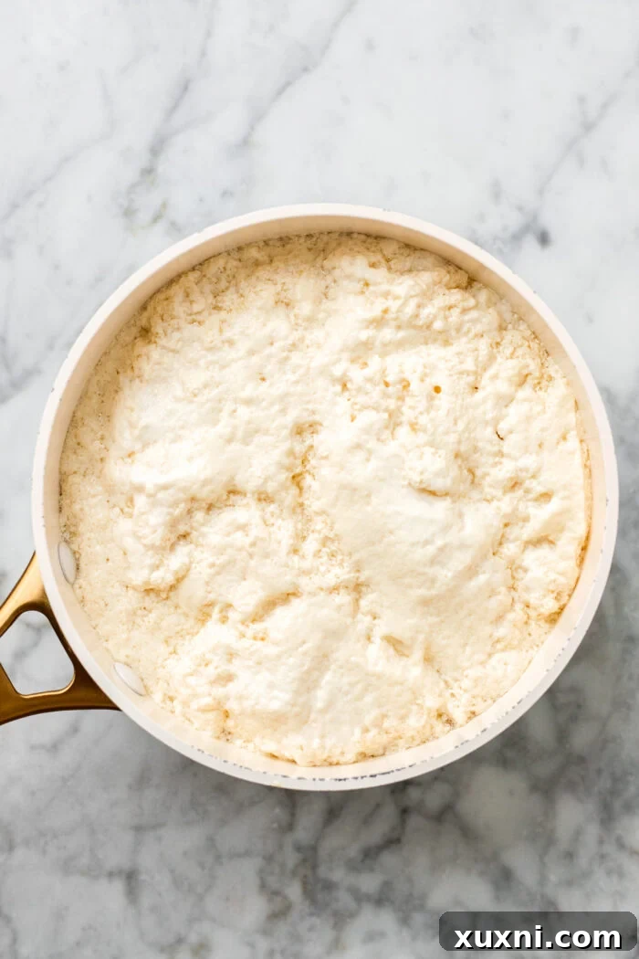 A close-up of boiled and curdled pea milk, showing the distinct separation of curds and whey in the saucepan.