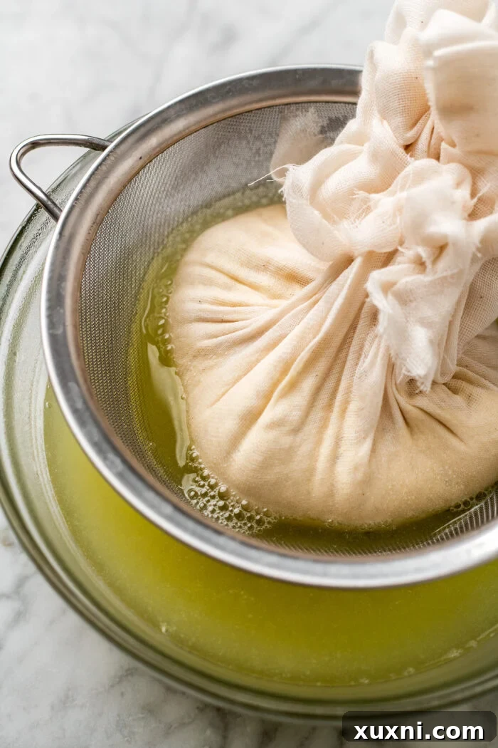 Hands squeezing excess liquid from the pea milk curds wrapped in cheesecloth, demonstrating the final straining process.