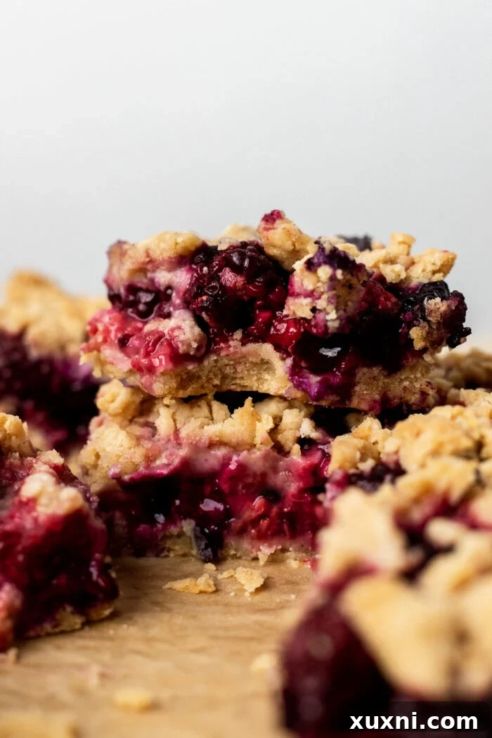 A close-up of a bitten triple berry crumble bar, showing the texture of the shortbread and the colorful berry filling.