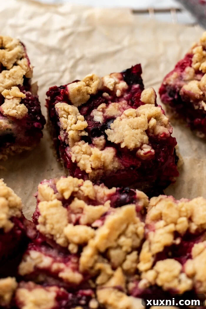 Close-up of baked triple berry crumble bars, showing the golden crumble topping and the vibrant, jammy berry filling underneath.