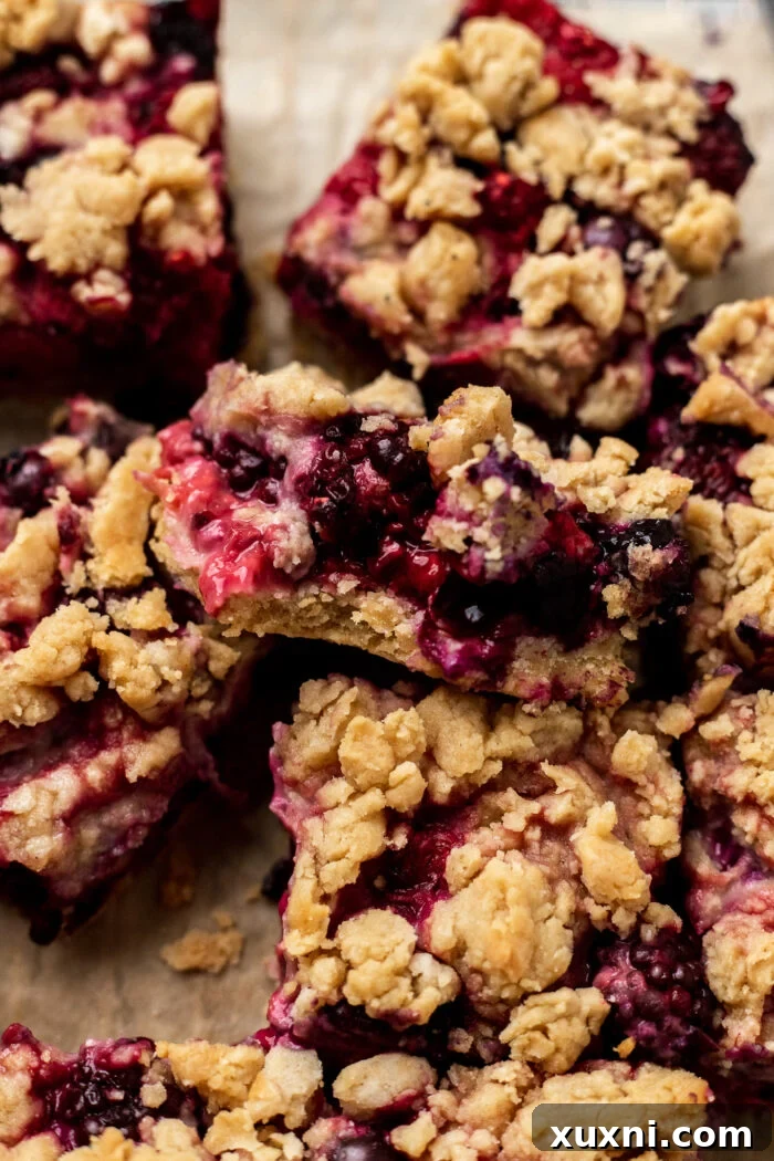 A hand holding a bitten triple berry crumble bar, revealing the luscious layers of berry filling and crumbly crust.