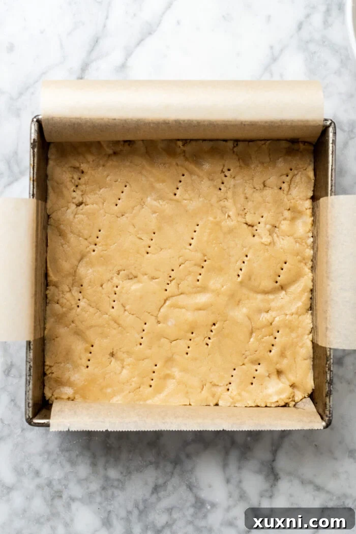 Poked shortbread crust in a baking pan, ready for its initial bake.