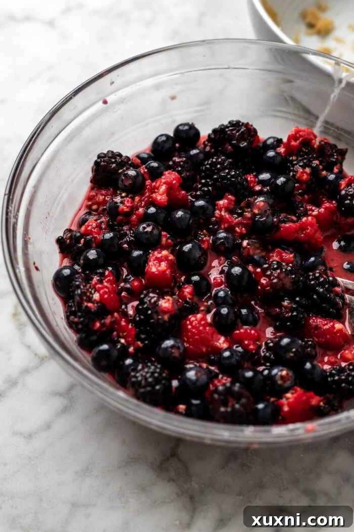 A bowl of mixed berries with cornstarch, lemon juice, and maple syrup, ready to be combined for the filling.