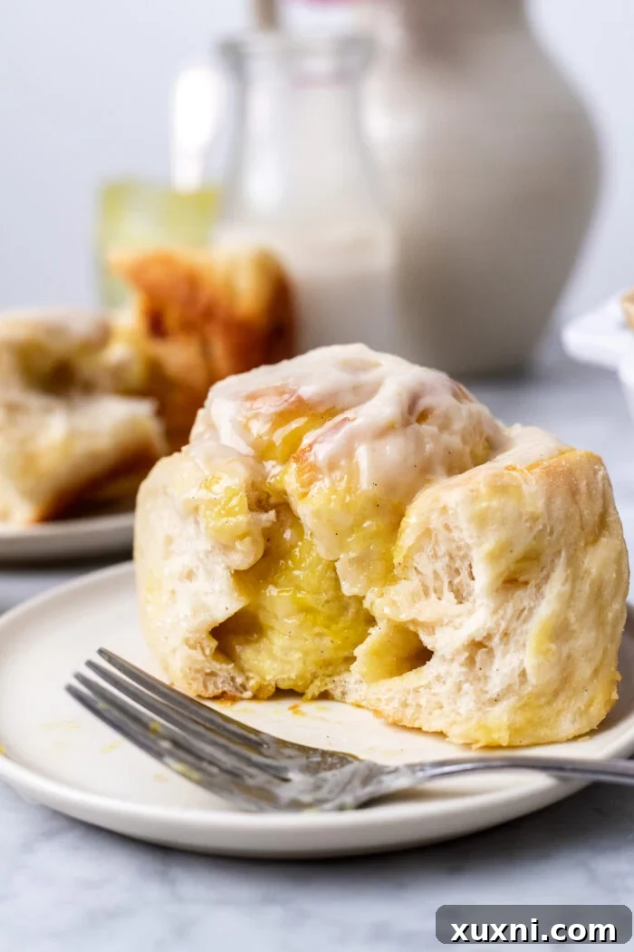 Small Batch Gooey Lemon Sweet Rolls Plant Based 2 A perfectly frosted vegan lemon sweet roll on a white plate, showcasing its soft texture and bright yellow curd peeking through.