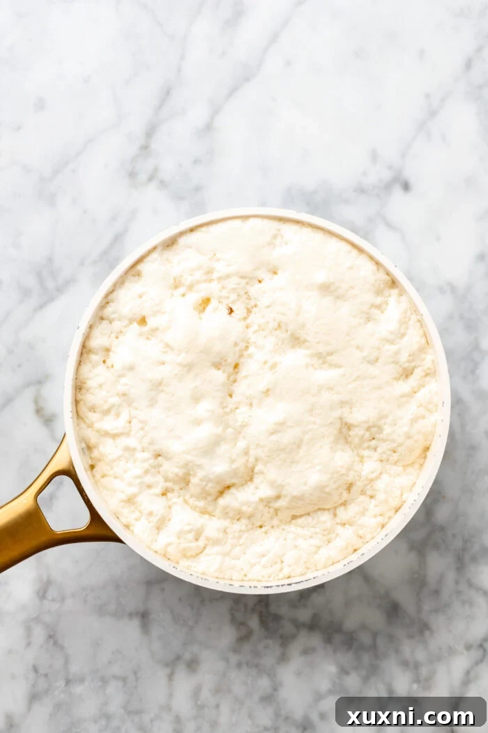 Close-up of bubbling and curdling pea milk in a saucepan, showing separated curds and whey.