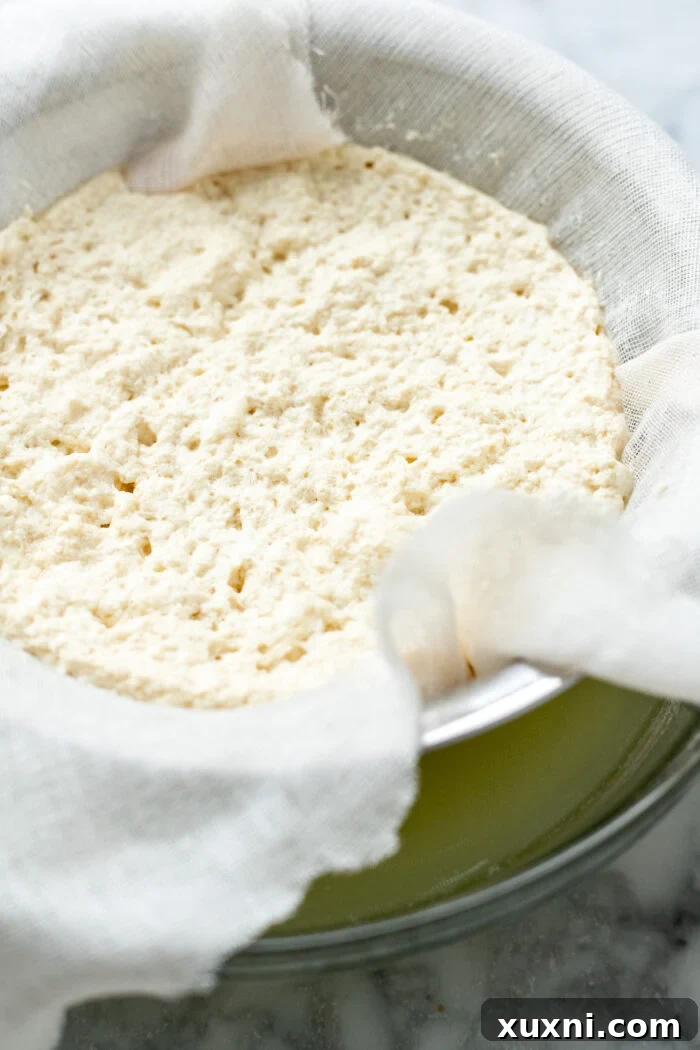 Straining the curdled pea milk through a cheesecloth-lined sieve, capturing the milk solids.