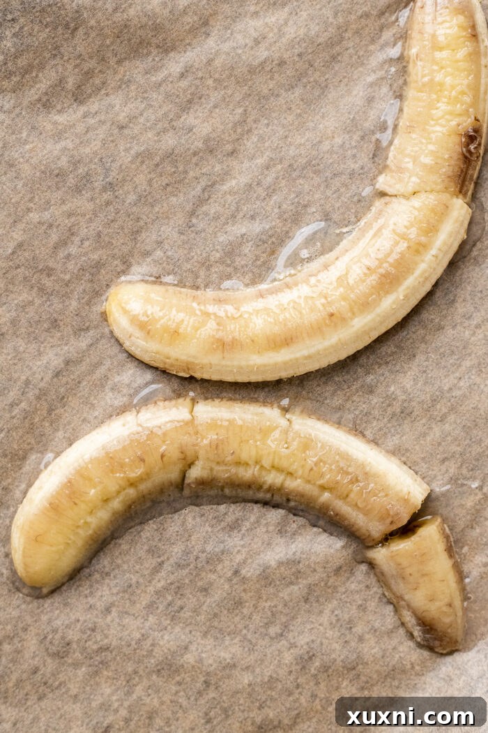 Roasted banana halves on a parchment-lined baking sheet, golden-brown and caramelized.