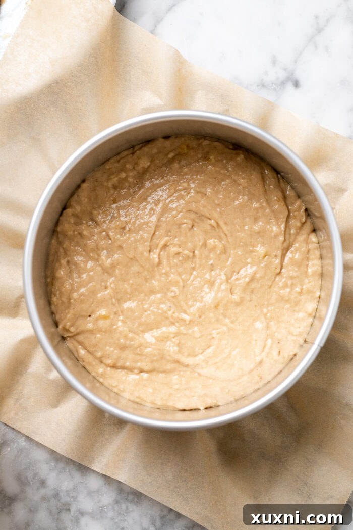 Half of the banana coffee cake batter spread in a round baking pan, ready for the filling.