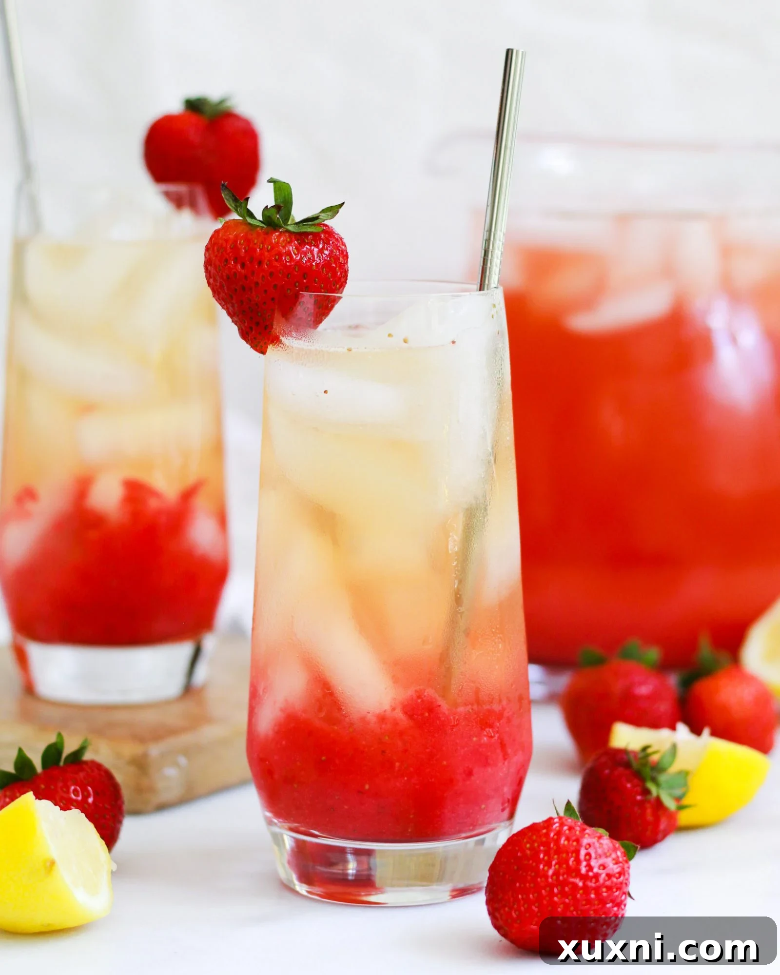 Pitcher and glasses of vibrant Iced Strawberry Green Tea Lemonade with fresh strawberries and lemon slices