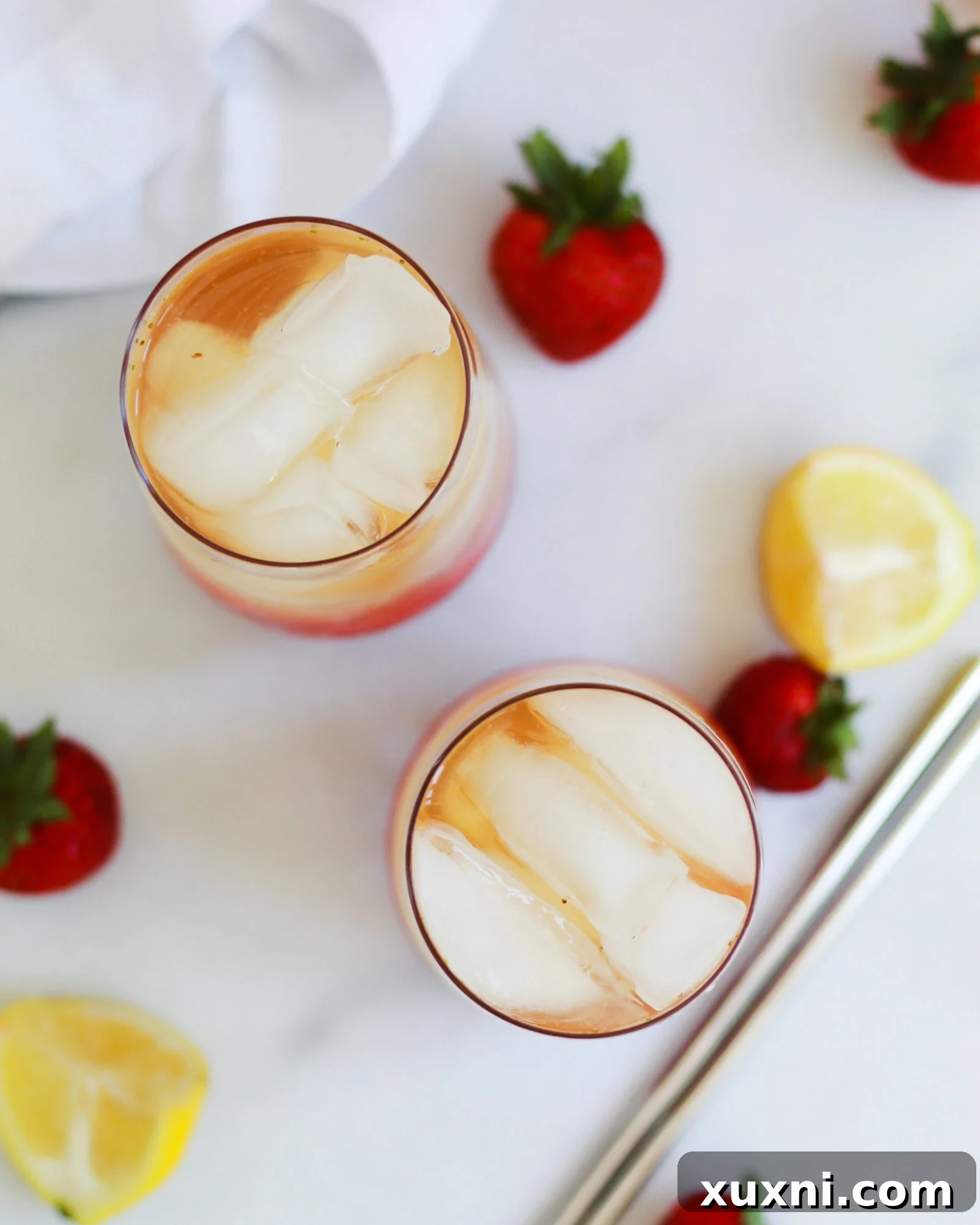 Overhead shot of two glasses of iced strawberry green tea lemonade adorned with fresh strawberries and lemon slices