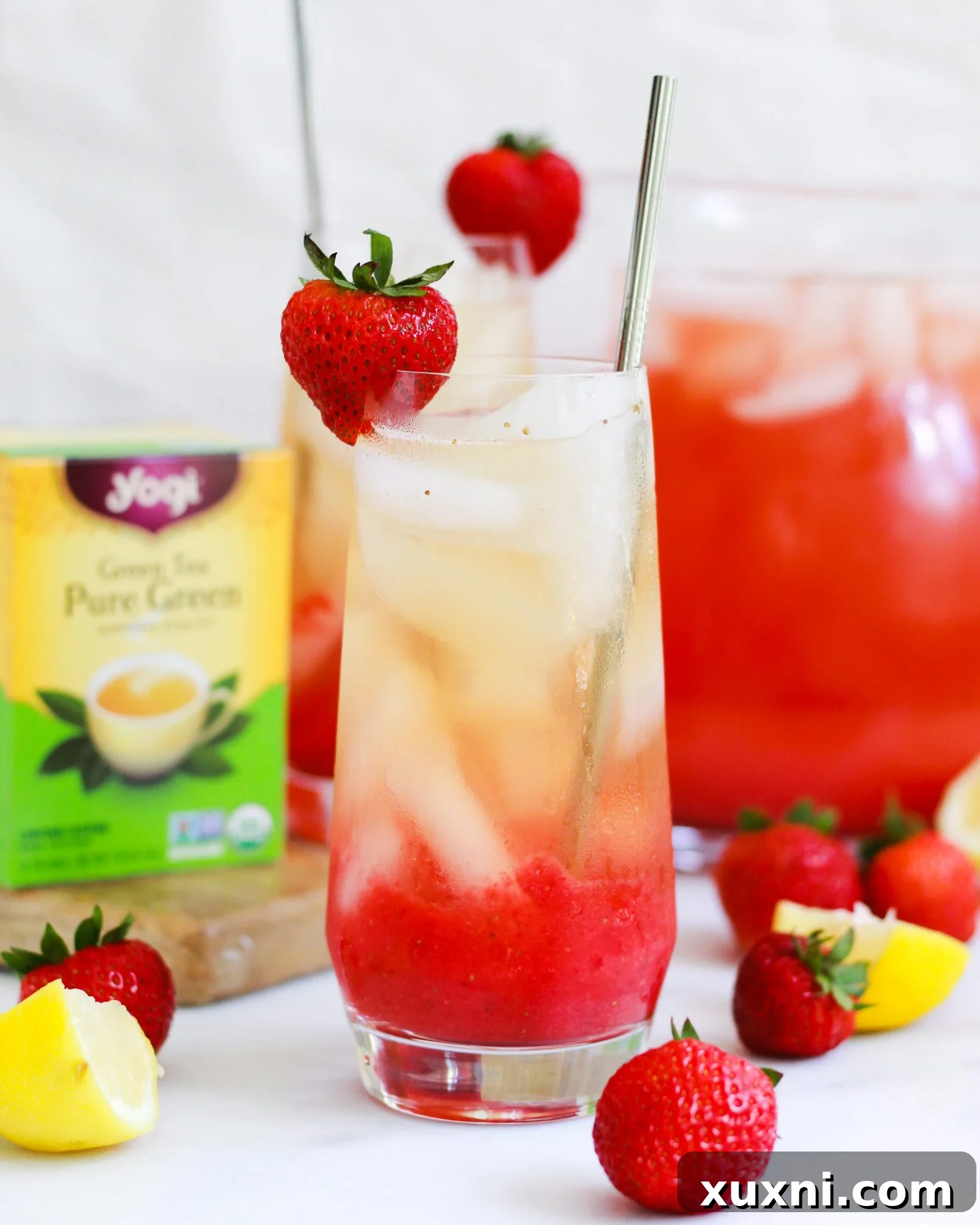 Iced Strawberry Green Tea Lemonade in a glass with a pitcher in the soft-focus background