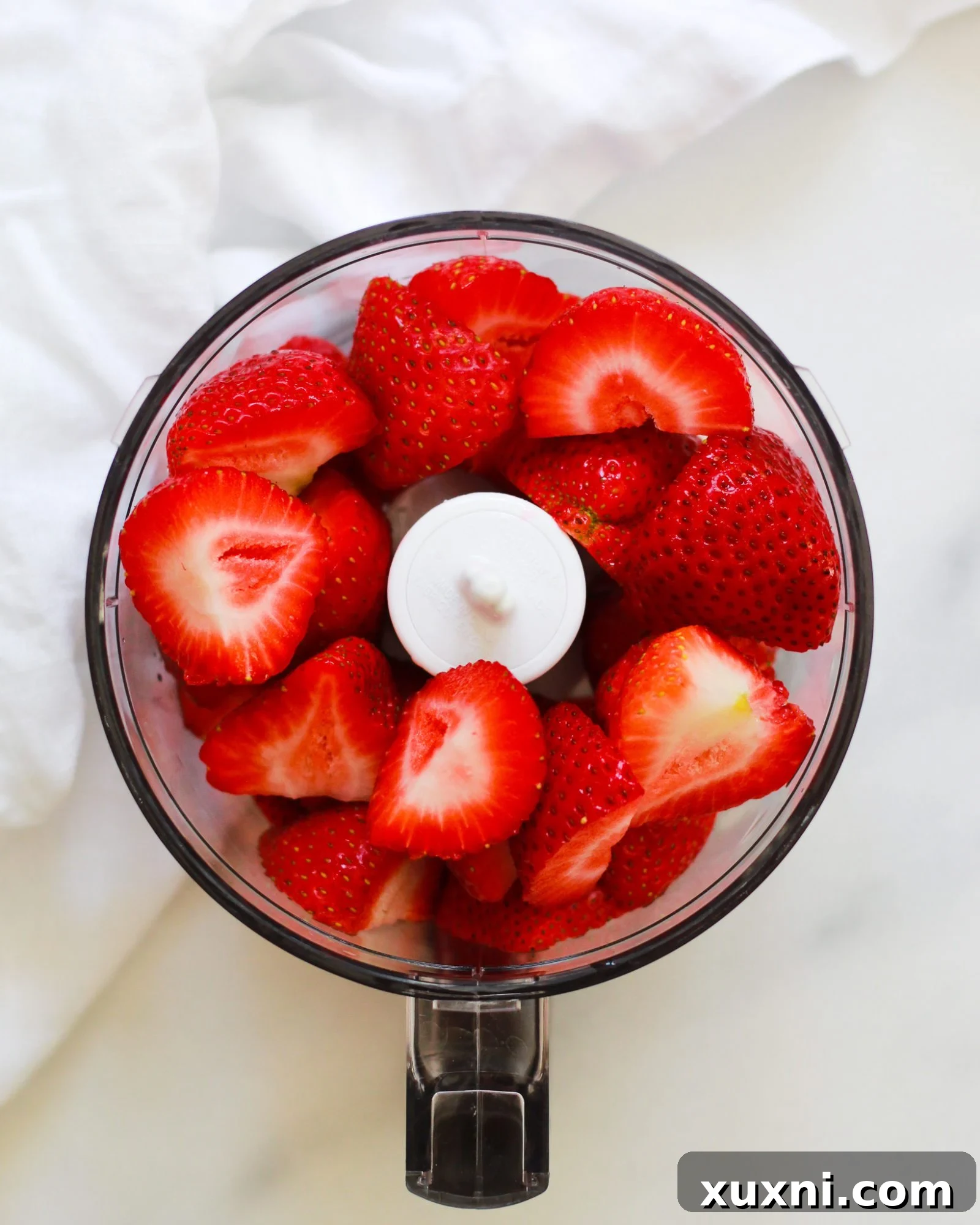 Whole, fresh strawberries being placed into a food processor for pureeing