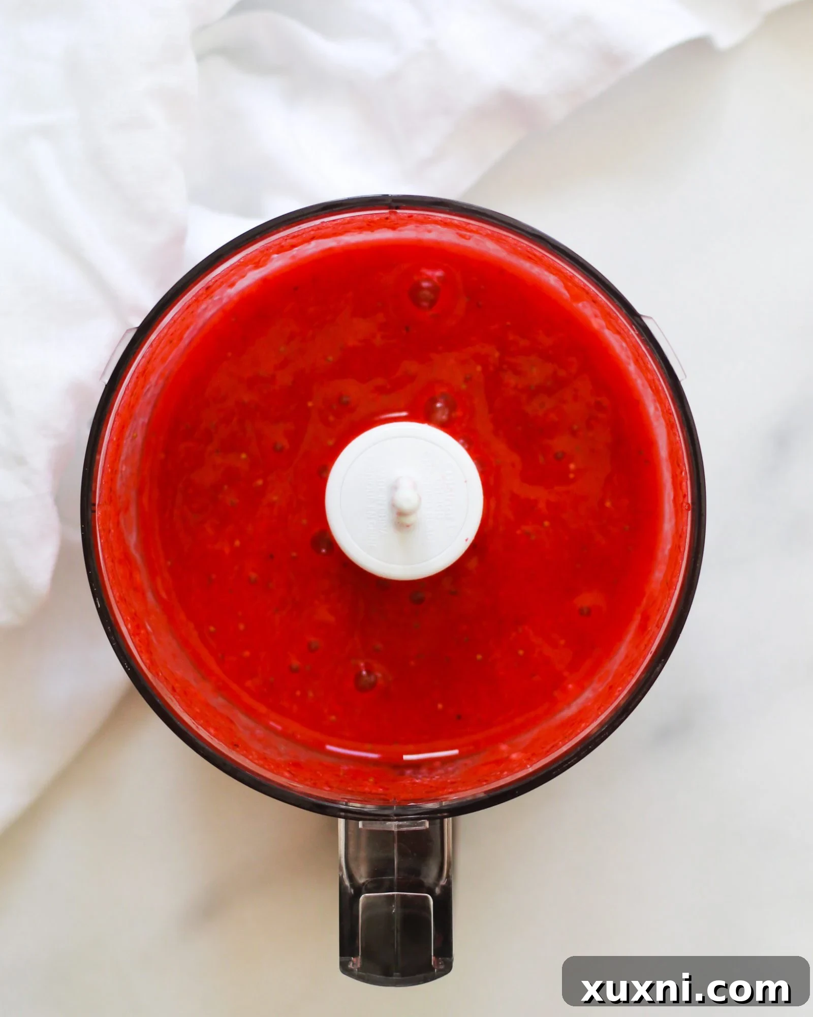 Smooth, bright red strawberry puree in a food processor, ready for straining