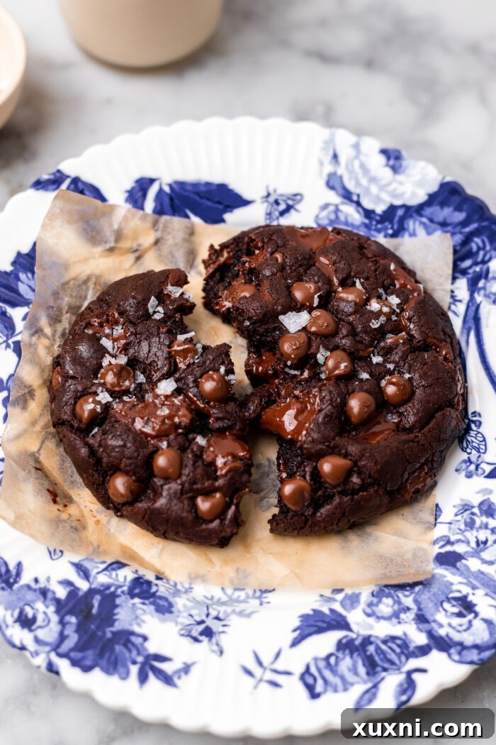 A rich, double chocolate chip cookie broken in half, revealing its gooey, molten center, served on a white plate.