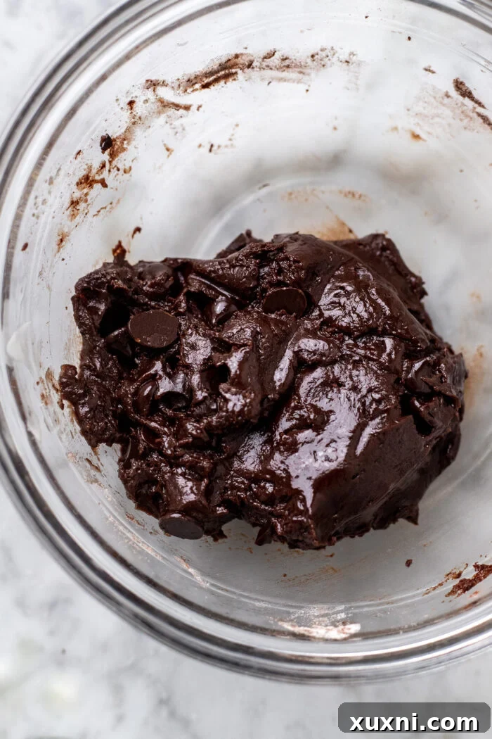 Folding in the dry ingredients, including flour, Dutch-process cocoa, baking soda, and salt, then adding chocolate chips to form the single serving cookie dough.
