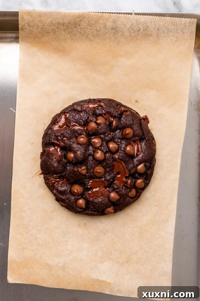 A freshly baked single serving double chocolate chip cookie on parchment paper, ready to be enjoyed with a sprinkle of sea salt.