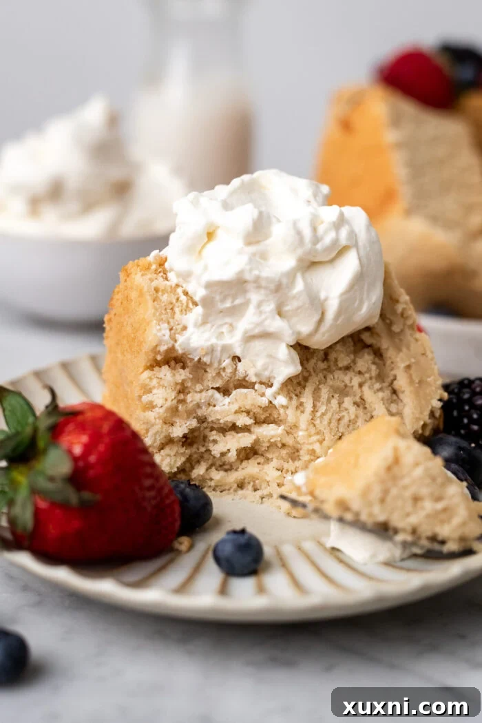 Heavenly Vegan Angel Food Cake 22 A delicate slice of vegan angel food cake, topped with a few fresh blueberries and raspberries, on a white plate.