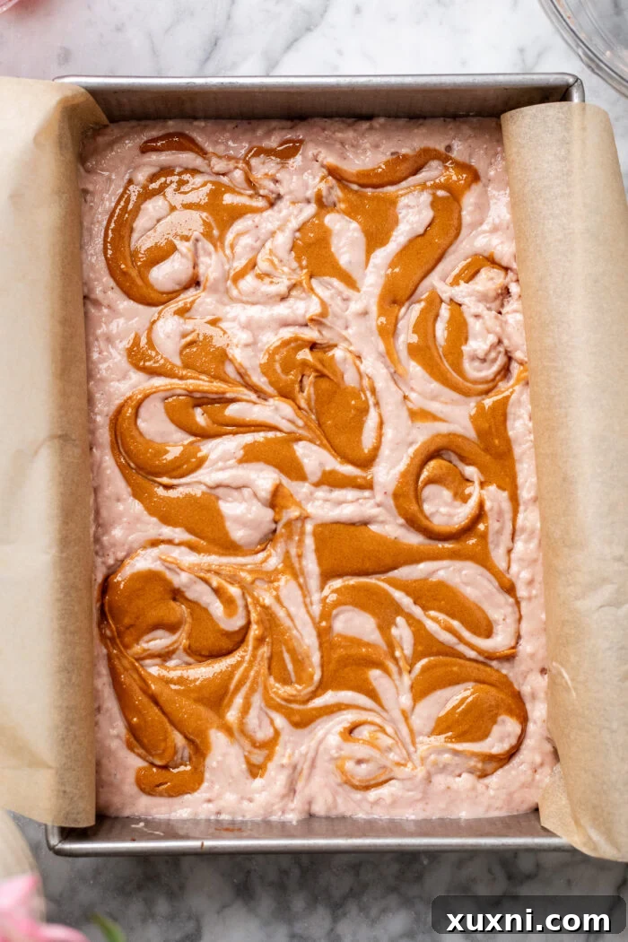 strawberry cake batter in a baking pan with peanut butter swirls on top, unbaked