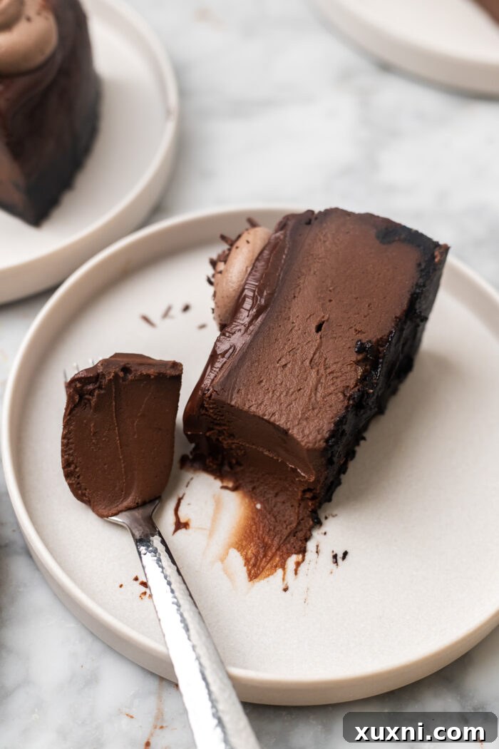 A single slice of vegan chocolate cheesecake on a white plate, showcasing its creamy texture and dark chocolate crust.
