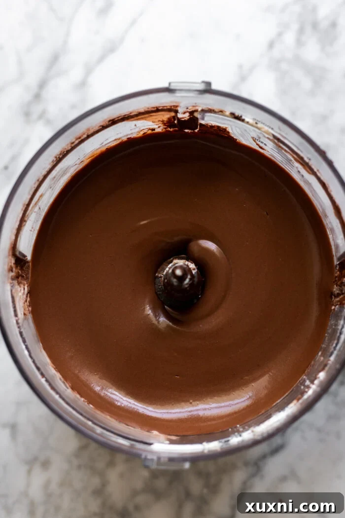 The smoothly blended vegan chocolate cheesecake batter inside a food processor, ready to be poured into the crust.
