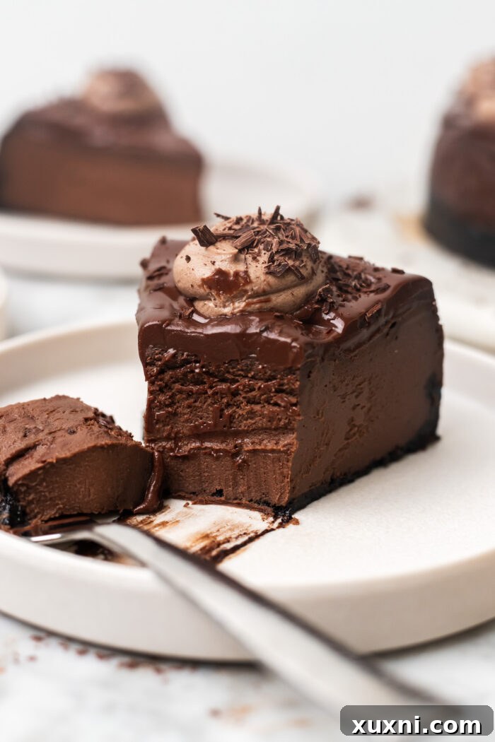 A close-up shot of a bitten slice of vegan chocolate cheesecake on a small plate, revealing its smooth, rich interior.