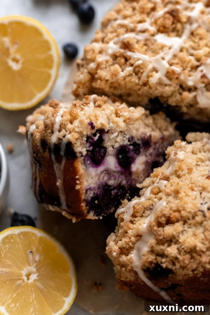 sliced vegan lemon blueberry coffee cake with lemons around it and a bowl of blueberries