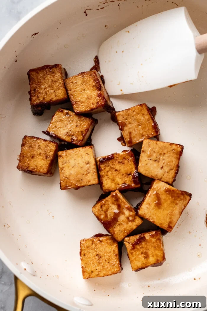 Tofu cubes being sautéed in a hot skillet with oil, developing a golden crust.