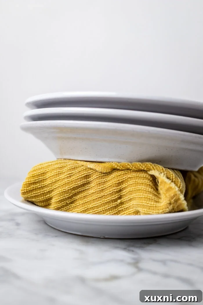 A block of extra-firm tofu being pressed between two plates with heavy books on top, demonstrating a DIY pressing method.