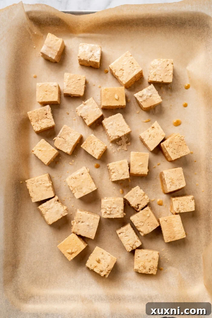 Marinated tofu coated in starch, spread on a parchment-lined baking sheet before baking.