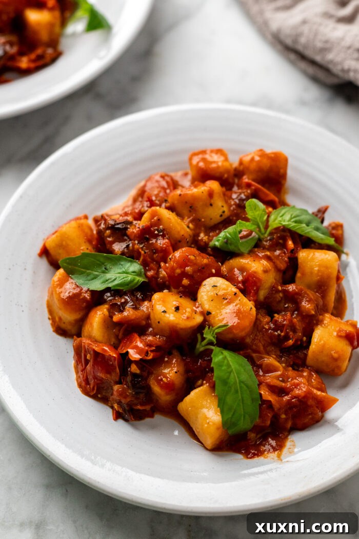 Plate of homemade vegan gnocchi pasta coated in vibrant burst cherry tomato sauce, ready to be served.