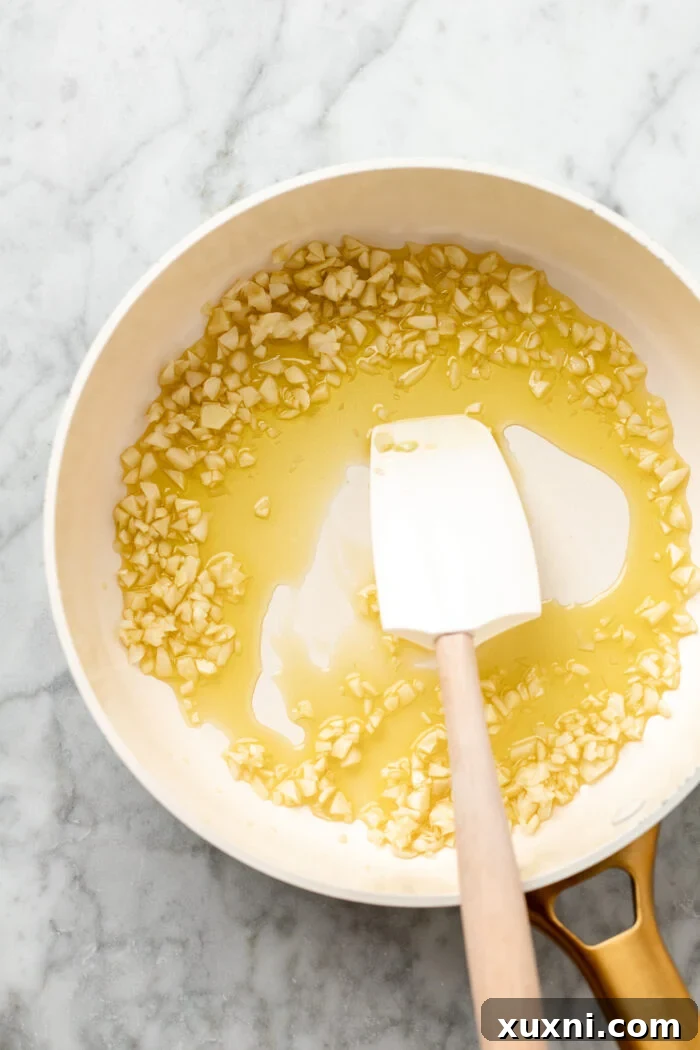 Minced garlic being sautéed in shimmering olive oil in a skillet.