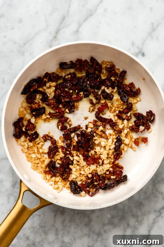 Chopped sun-dried tomatoes added to the pan with garlic and olive oil, ready to be covered.