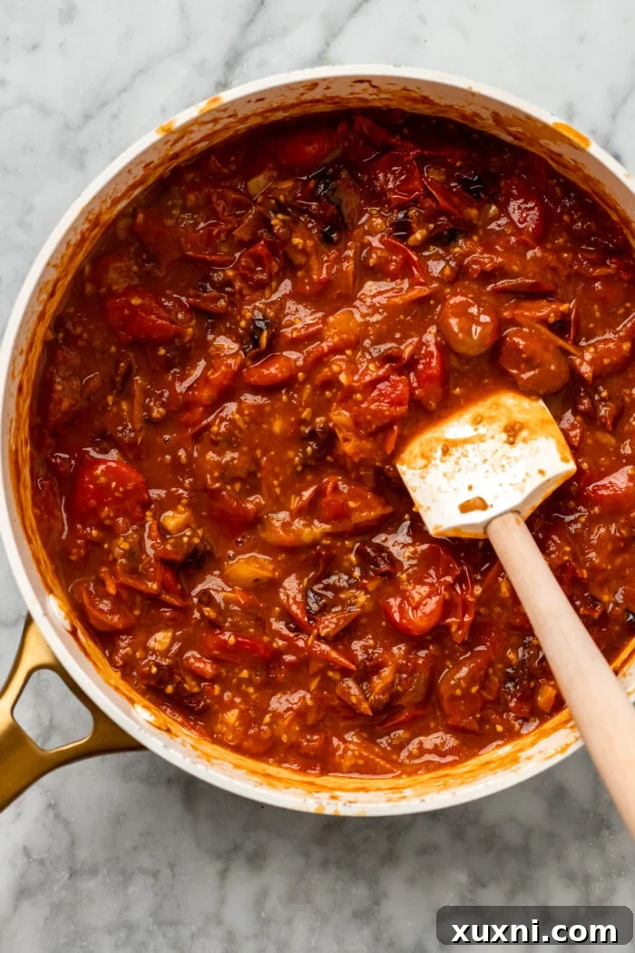 Vibrant, chunky cherry tomato sauce simmering gently in a pan after the tomatoes have burst.