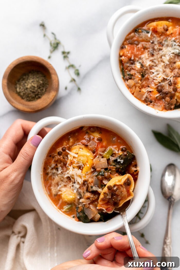 A close-up shot of a hand gently scooping a spoonful of vegan tortellini soup from a rustic bowl, highlighting the perfectly cooked tortellini and wilted kale.