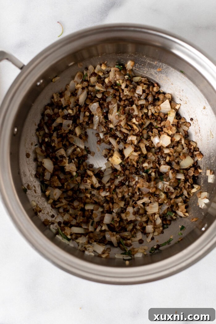 Cooked lentils, fresh thyme, sage, paprika, cumin, and red pepper flakes being added to the sautéed onions and garlic in a pot, ready to be stirred and infused with flavor.