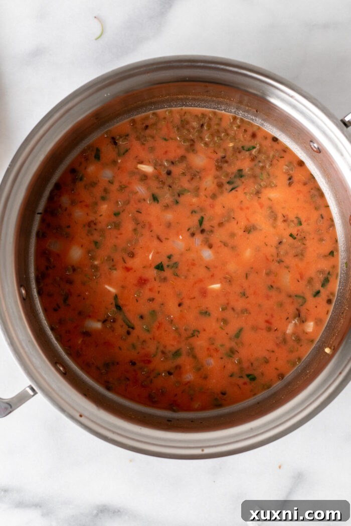 Crushed tomatoes, vegetable stock, and cashew cream being poured into the pot with the sautéed ingredients, creating the rich and creamy base for the vegan tortellini soup.