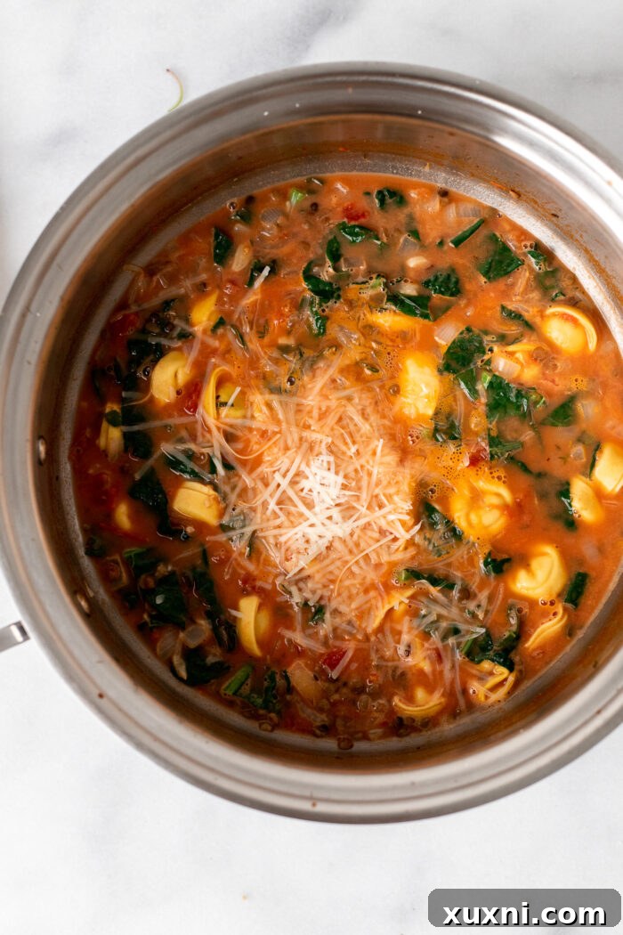 Vegan tortellini and fresh kale added to the simmering creamy tomato broth, stirring gently to combine before the final few minutes of cooking.