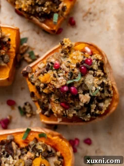Roasted and stuffed butternut squash halves on a baking sheet, garnished with fresh herbs and pomegranate seeds.