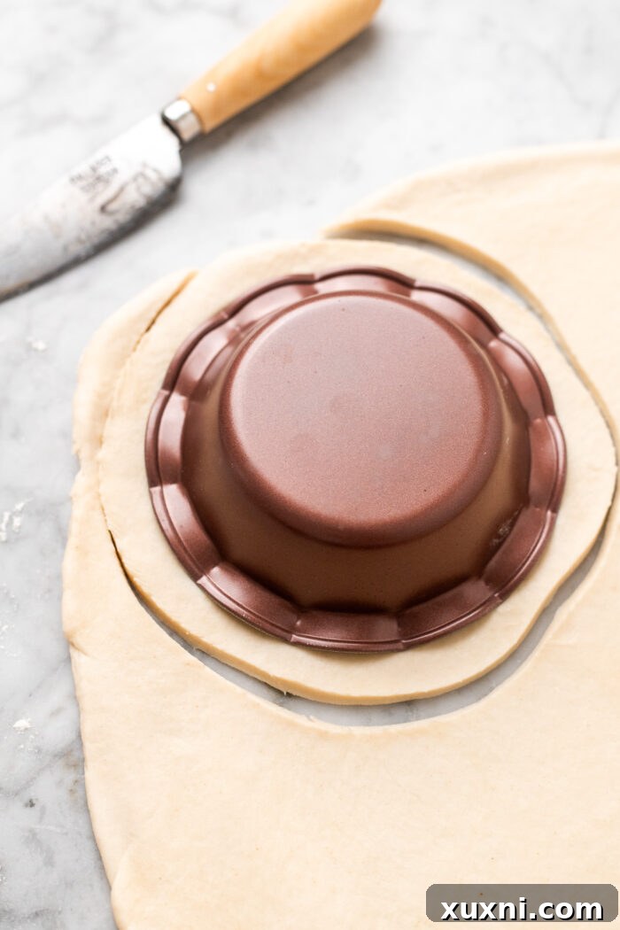 A hand gently shaping rolled-out pie dough against a 5-inch mini pie dish, preparing to cut the perfect circle.