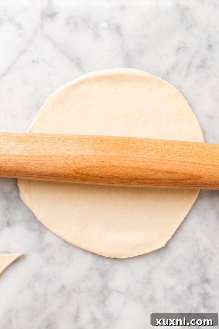 A rolling pin gliding over pie dough, demonstrating how to achieve a wider, thinner circle if needed.