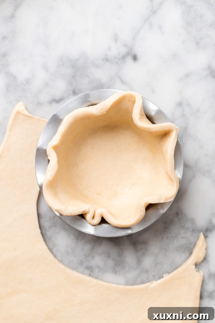 Hands carefully pressing a circular piece of pie dough into a 5-inch mini pie pan, forming the crust.