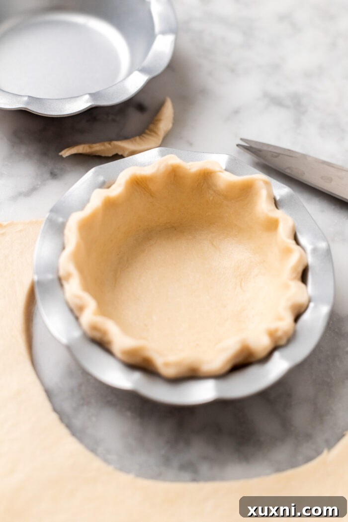 Close-up of a meticulously shaped pie crust rim within a mini pie dish, ready for chilling.